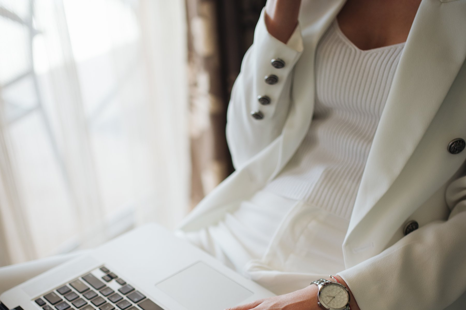 personne en tenue professionnelle assise près d'une fenêtre, une main posée sur le clavier d'un ordinateur portable