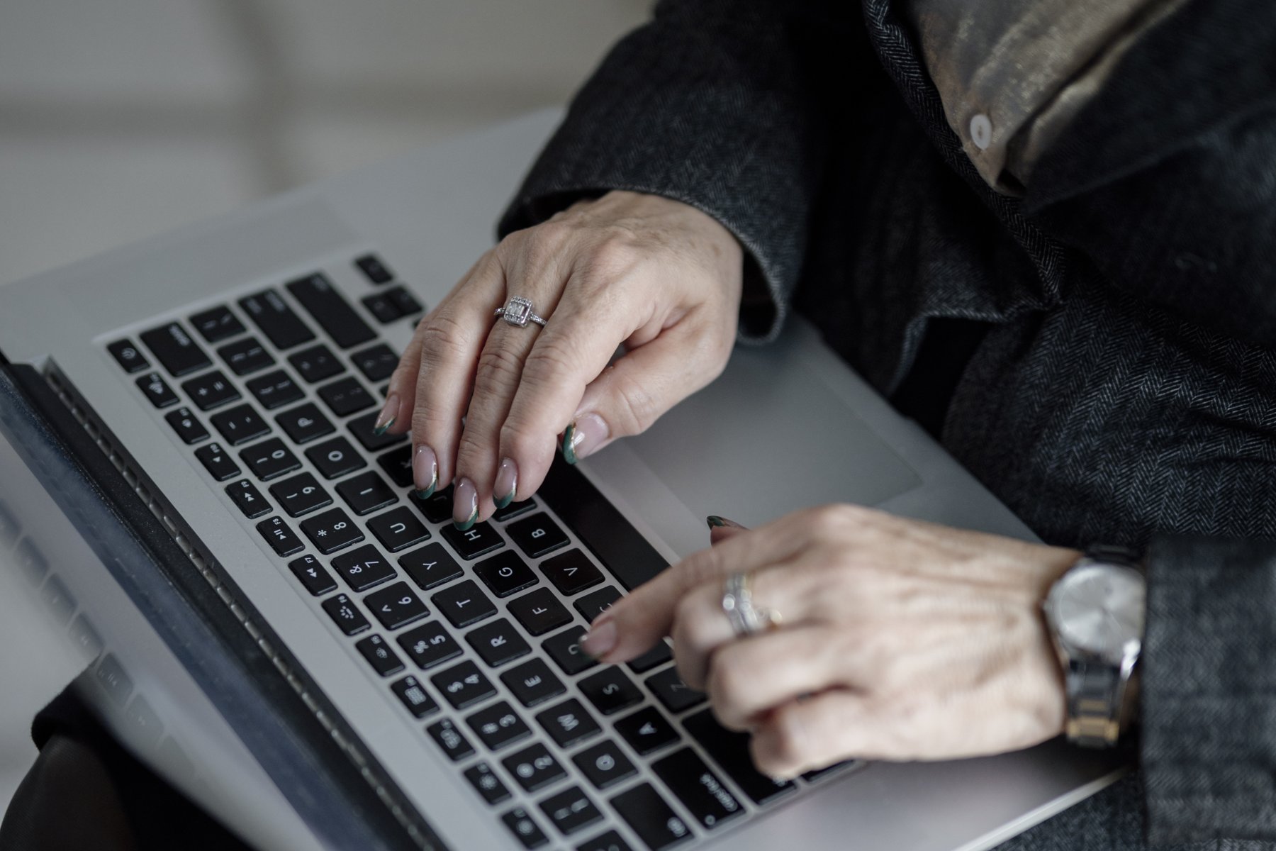 mains qui tapent sur le clavier d'un ordinateur portable, bagues et montre visibles