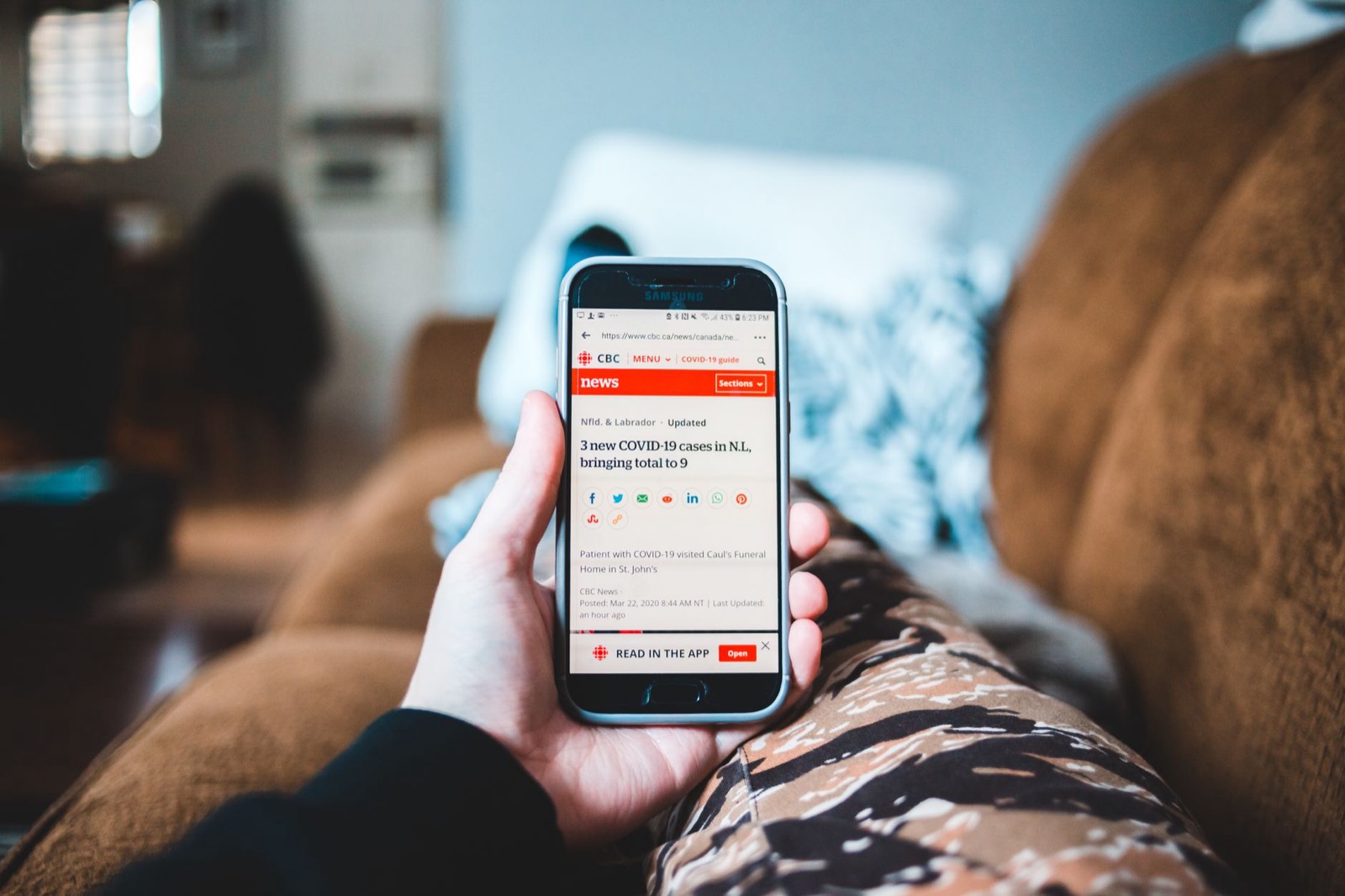 Mains tenant un smartphone affichant un site d'actualité, lecture des titres et des dates de publication