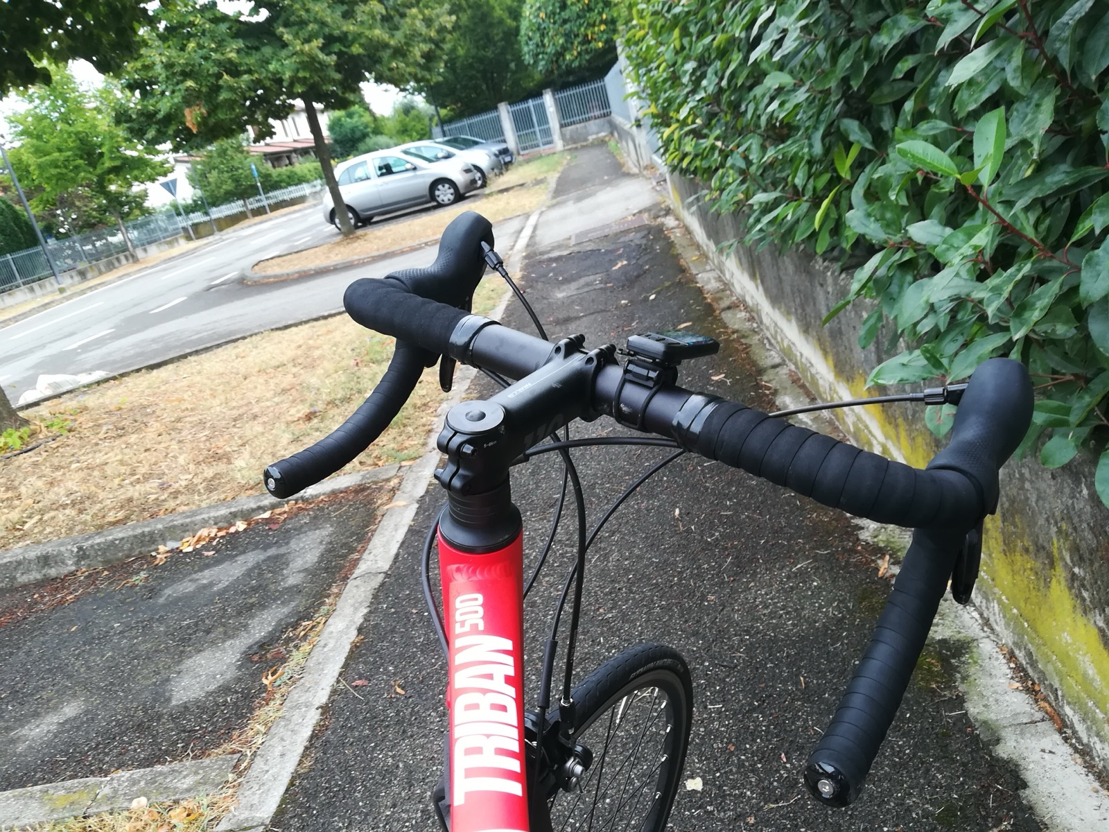 Cintre et potence d'un vélo de route Triban 500 vus depuis la selle, sur une piste cyclable bordée d'une haie